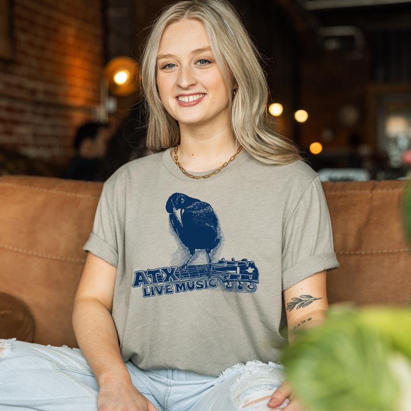 Model wearing ATX Crow T-shirt with crow and guitar graphic, representing Austin’s live music scene