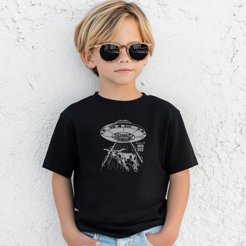 Child wearing a black t-shirt with a UFO graphic against a textured white wall.