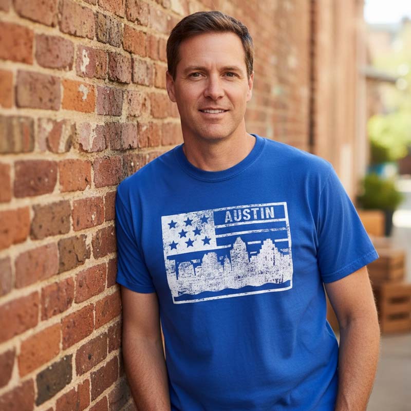 Man wearing a blue t-shirt with 'Austin' design leaning against a brick wall.
