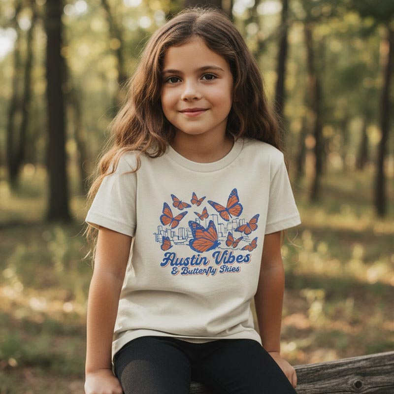 Young girl wearing a 'Austin Vibes & Butterfly Fries' t-shirt in a forest setting