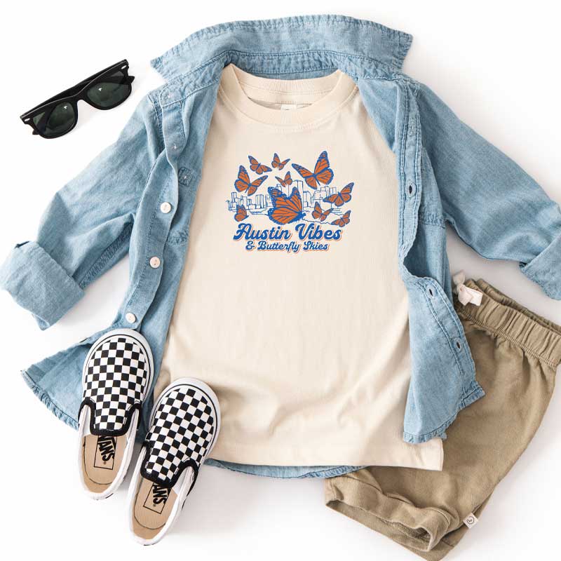 Casual outfit with denim shirt, t-shirt with graphic design, shorts, and checkered shoes on a white background