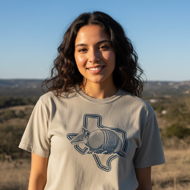 Woman wearing a t-shirt with a Texas-shaped armadillo design in a desert landscape.