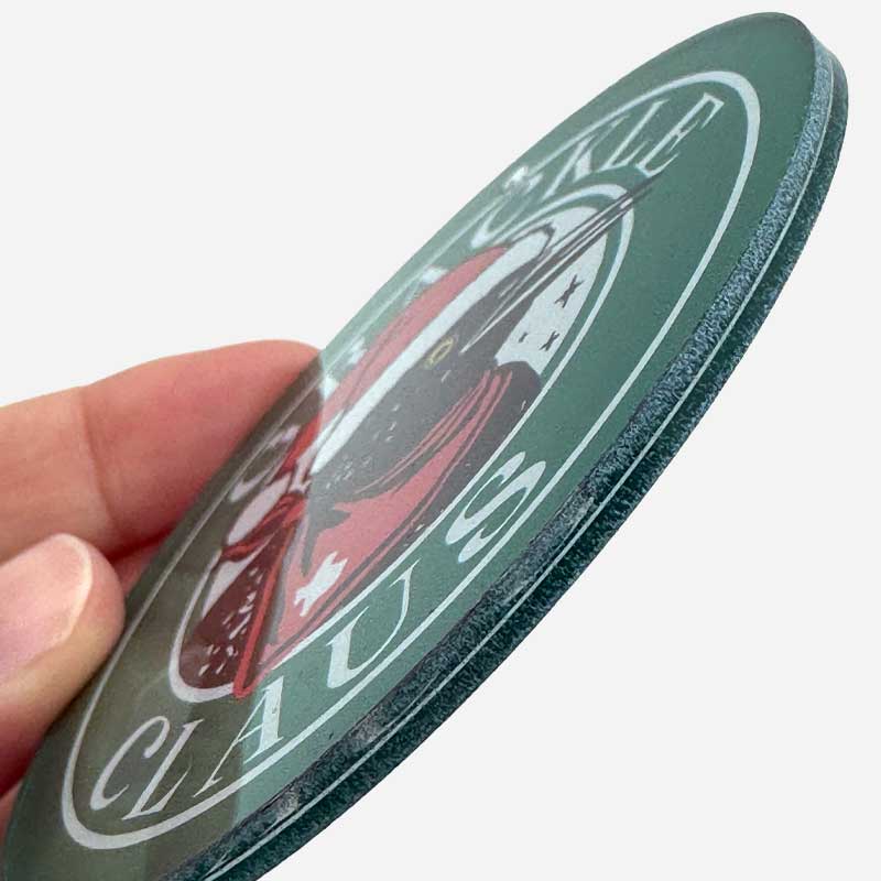 Circular object with a design and 'Claus' text held by a hand on a white background