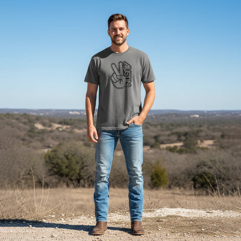 Man wearing a gray t-shirt with a peace sign design and 'Austin' text, standing in a scenic outdoor setting.