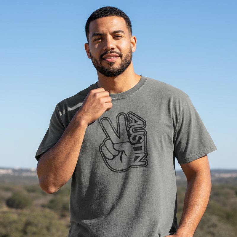 Man wearing a gray t-shirt with a peace sign and 'Austin' design, standing outdoors against a clear blue sky.