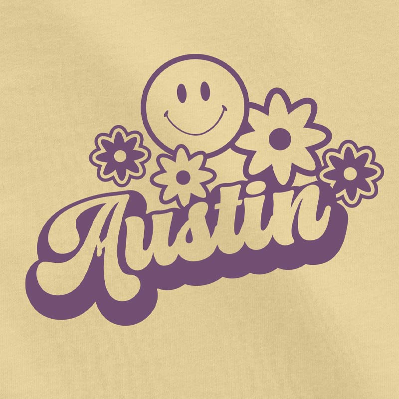 Close-up of the Hippie Austin graphic in bright purple ink on soft butter-yellow toddler cotton tee, showing smiley and flower details.