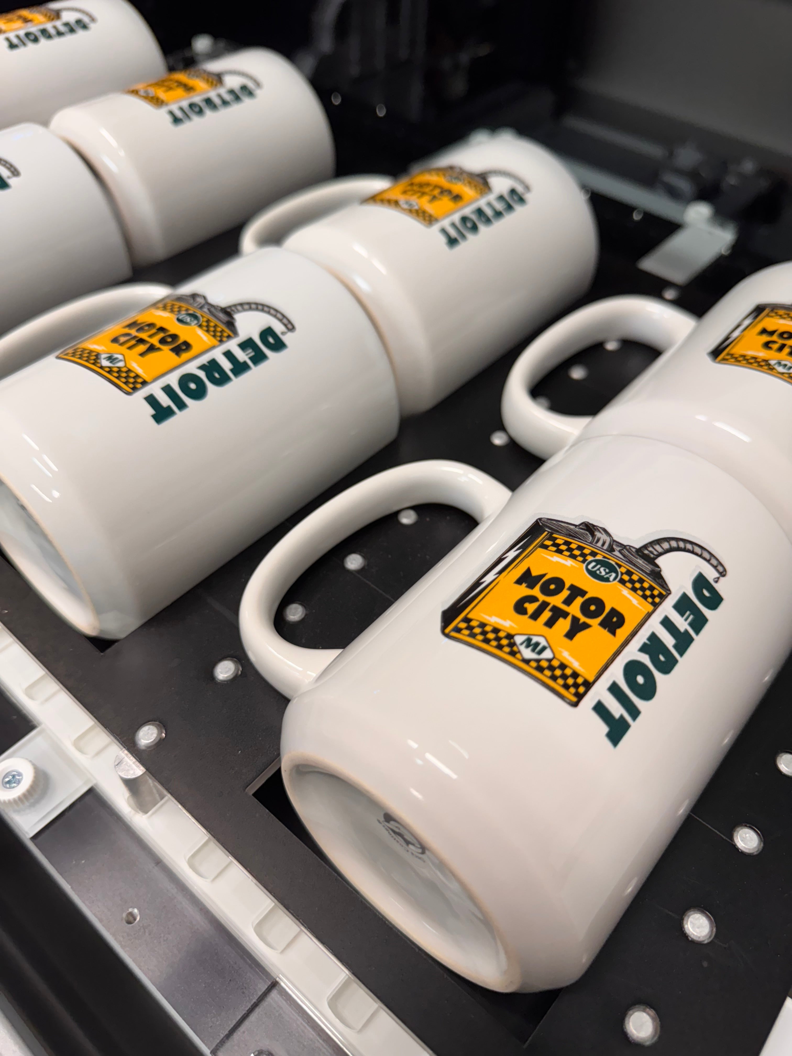 White mugs with 'Detroit' and tiger logo on a black background
