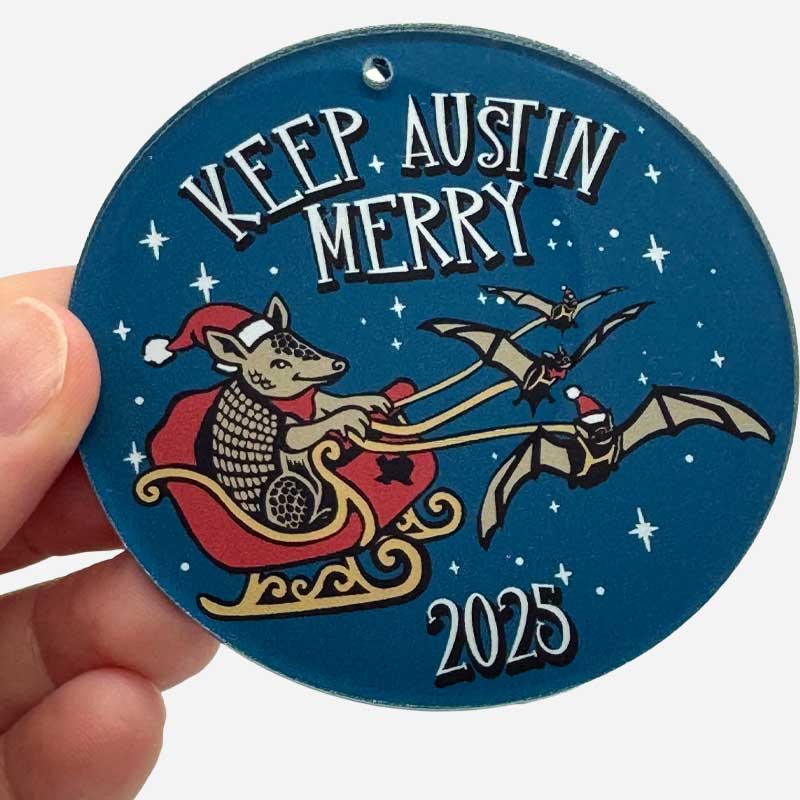 Circular ornament with 'Keep Austin Merry' text and festive design, held by a hand.