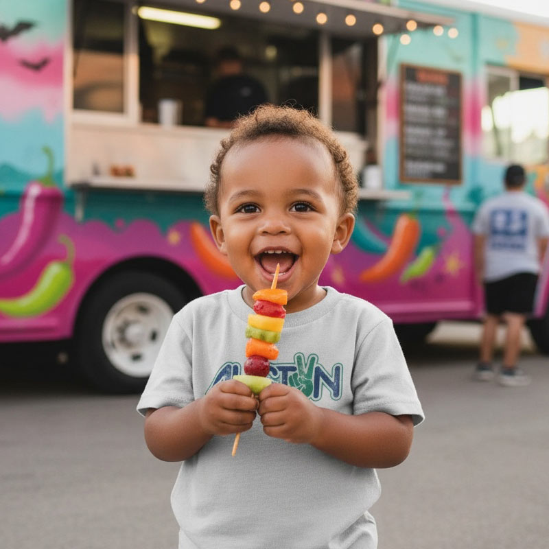 Child holding a colorful skewer in front of a vibrant food truck.