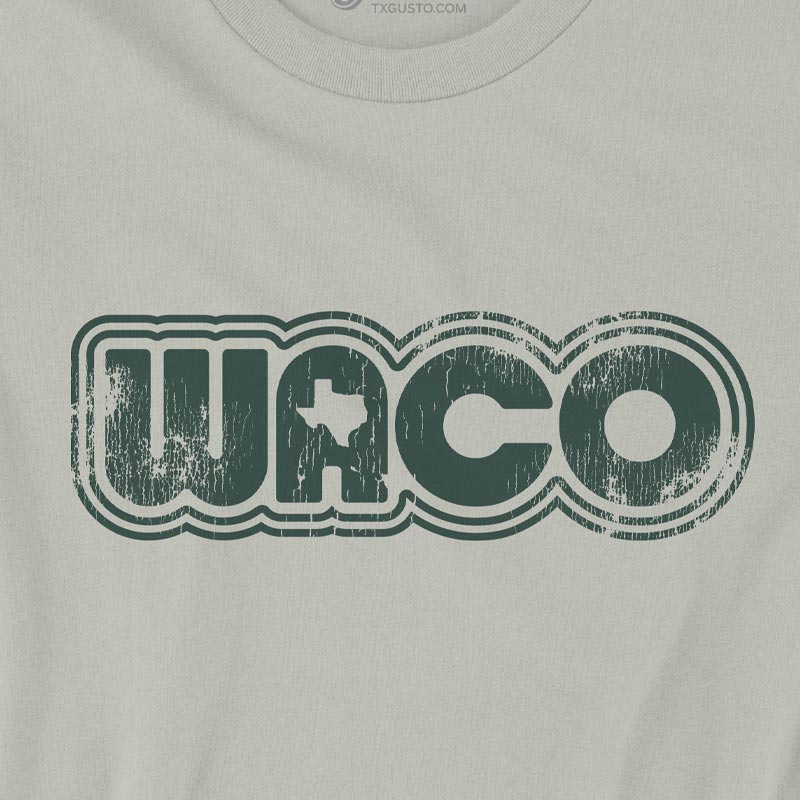 Unisex soft thyme green Retro Waco graphic T-shirt. Design features bold retro lines spelling “Waco” with a tiny Texas silhouette inside the “A.”