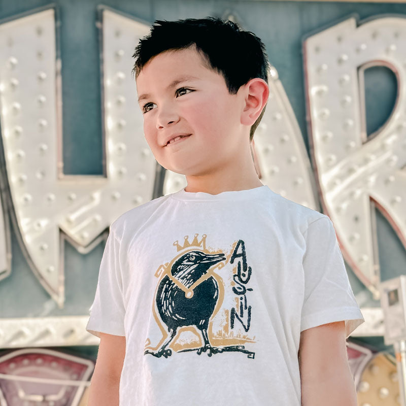 Child wearing a white t-shirt with a graphic design in front of vintage sign letters.