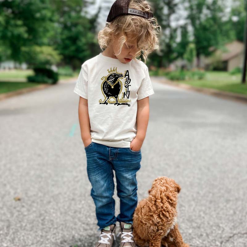 Toddler wearing Royal Squawk Austin t-shirt featuring a crown-wearing grackle – cute and fun ATX tee for kids