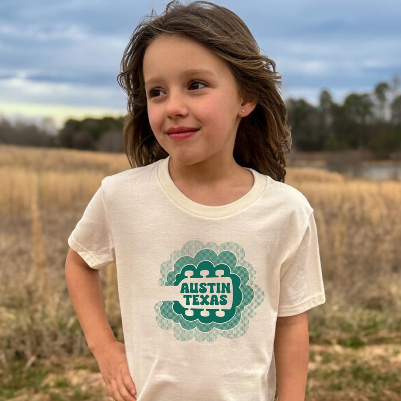 Model wearing our Sky Sync youth t-shirt with guitar neck rising into clouds – Austin music-themed tee for kids
