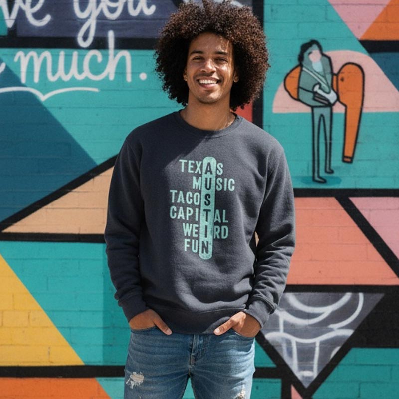 Person wearing a sweatshirt with text standing in front of a colorful mural.