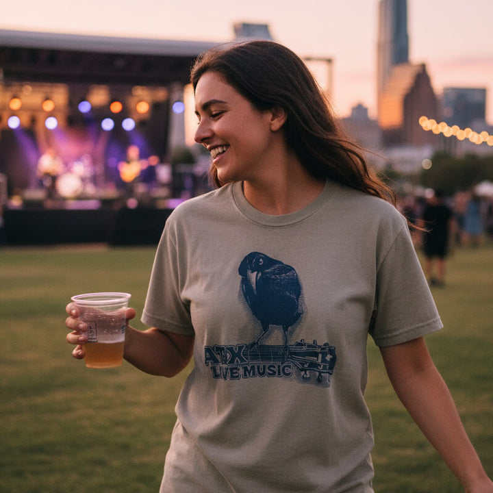 Woman at a live music event holding a drink, wearing a t-shirt with a graphic design.