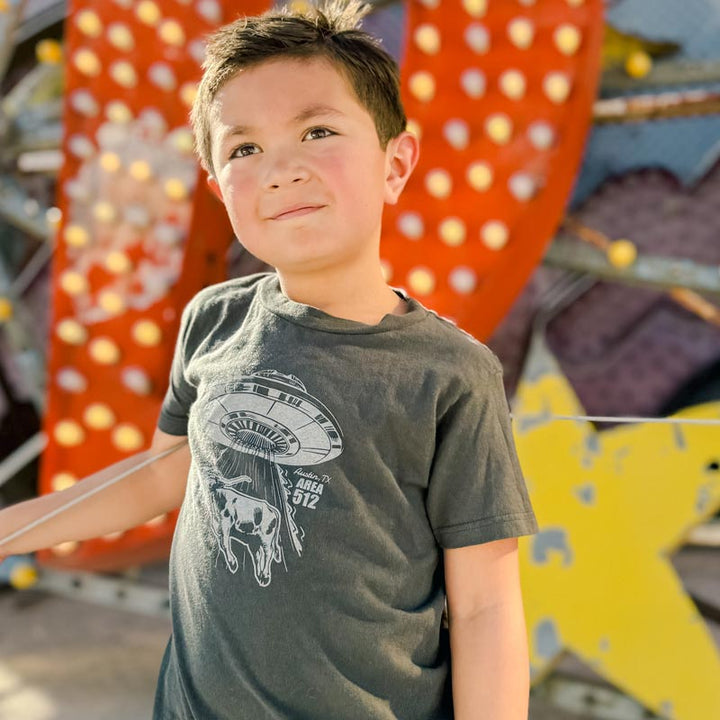 Young boy wearing a t-shirt with a graphic of a space ship with a longhorn cattle, standing in front of colorful outdoor decorations.
