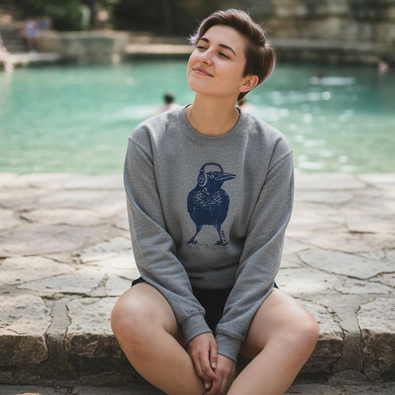 Person wearing a gray sweatshirt with a blue graphic, sitting by a pool.