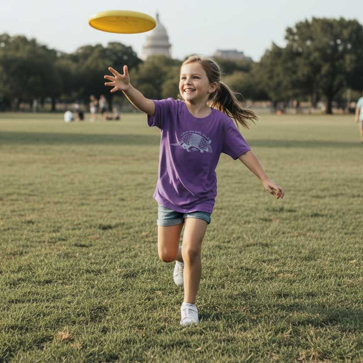 Girl in a purple shirt running with a yellow frisbee in a park