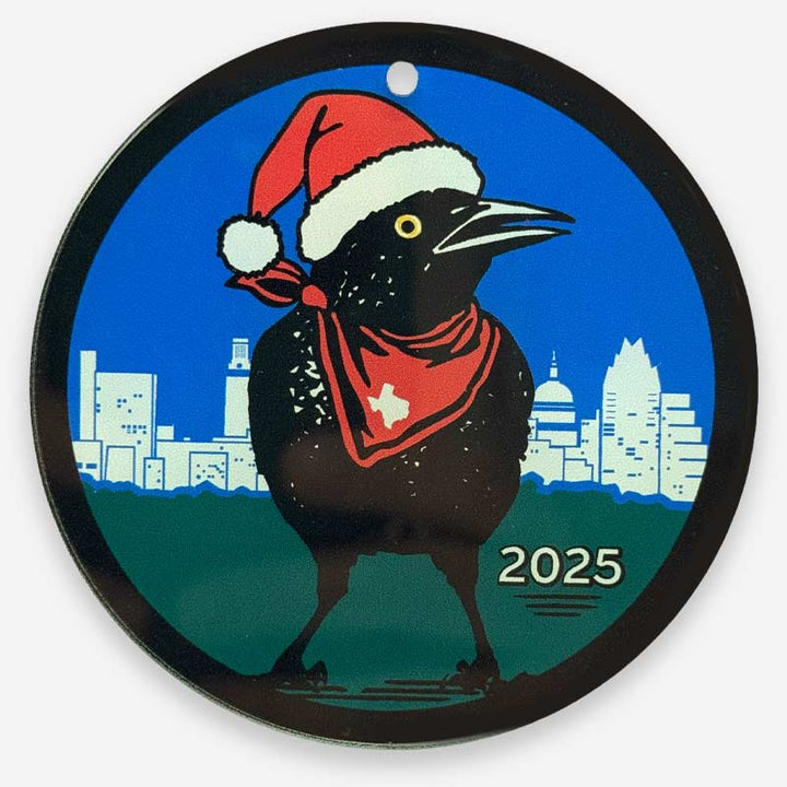 Circular ornament with a Grackle bird wearing a Santa hat and red bandana, city skyline, and &