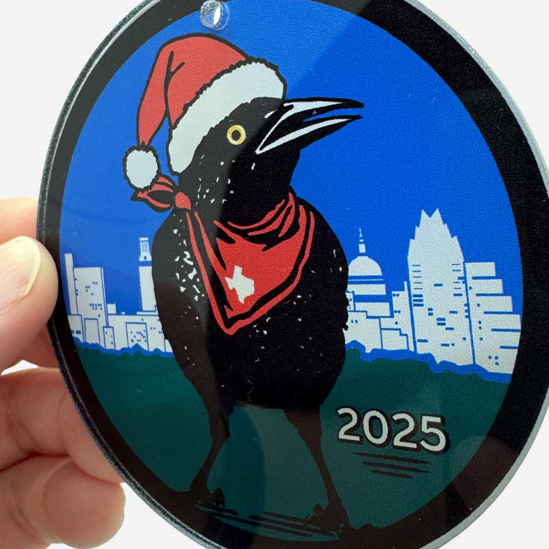 Circular ornament with a bird wearing a Santa hat and a cityscape in the background, featuring the year 2025.