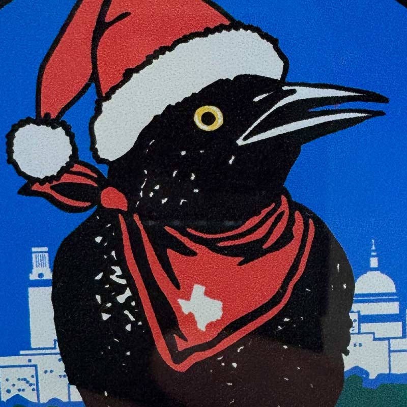 Grackle bird wearing a Santa hat and red bandana with Texas design on a blue background