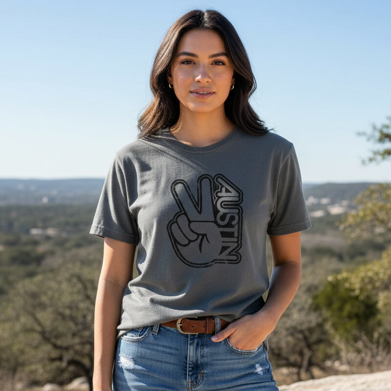 Woman wearing a gray t-shirt with a peace sign and 'Austin' design, standing outdoors.