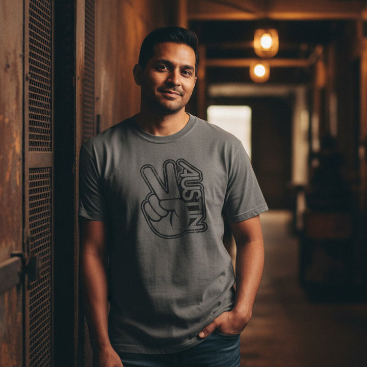 Man wearing a gray t-shirt with a peace sign and 'Austin' text, standing in a dimly lit hallway.