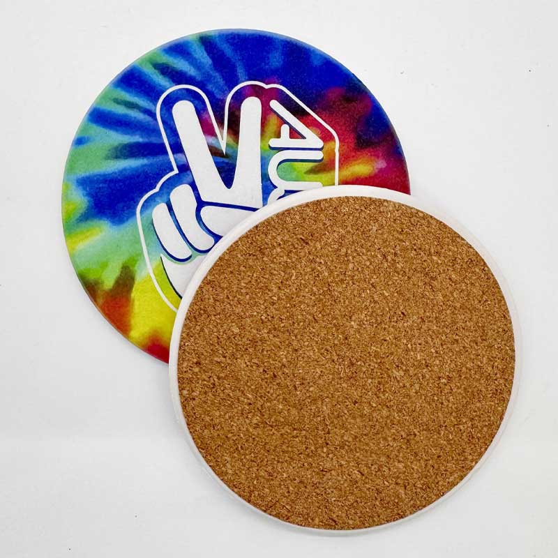 Two round coasters, one tie-dye with a peace sign design, the other brown cork, on a white background.