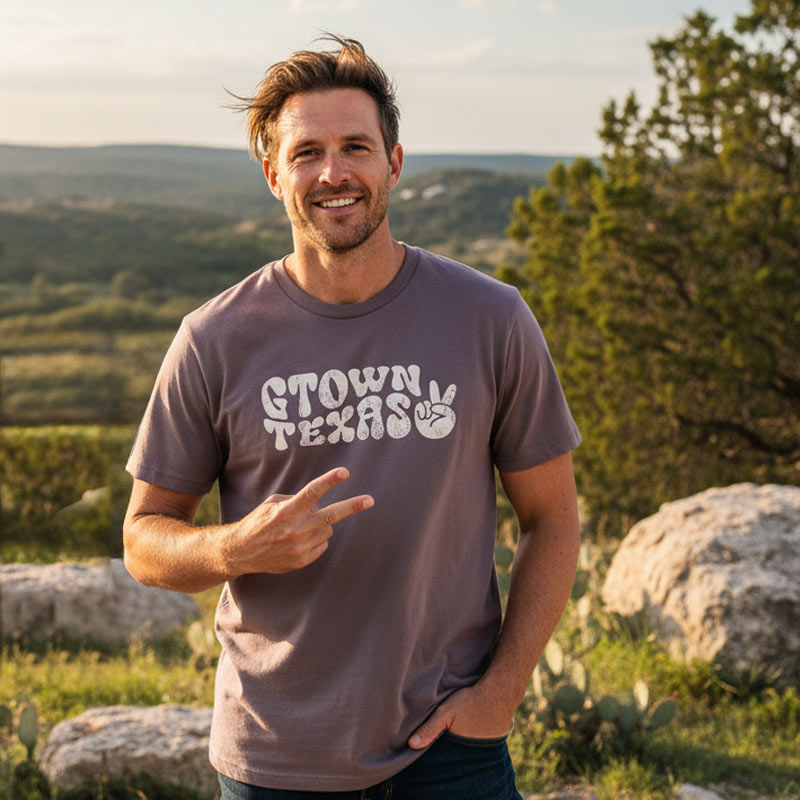 Man wearing a 'Gtown Texas' t-shirt standing outdoors with a scenic background