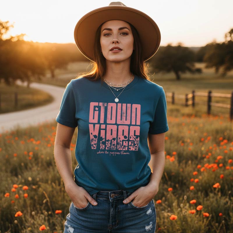 Woman wearing a blue t-shirt with pink text in a field of flowers during sunset.
