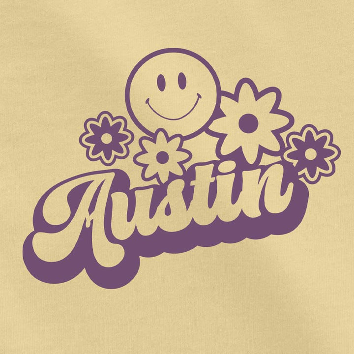 Close-up of the Hippie Austin graphic in bright purple ink on soft butter-yellow toddler cotton tee, showing smiley and flower details.