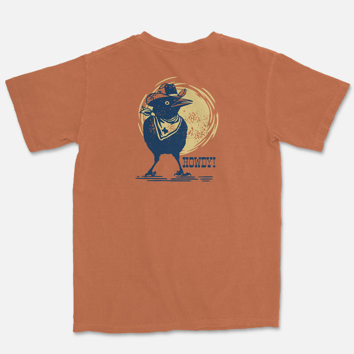 Orange t-shirt with a graphic of a grackle bird in a cowboy hat and 'Howdy!' text on a white background
