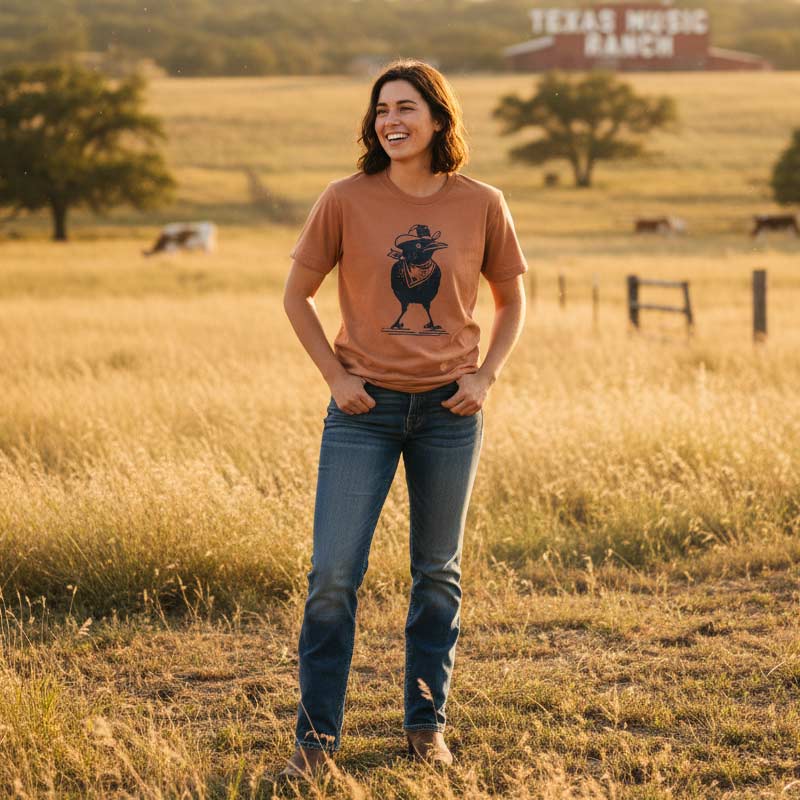 Woman standing in a field wearing a brown t-shirt with a graphic design, smiling.