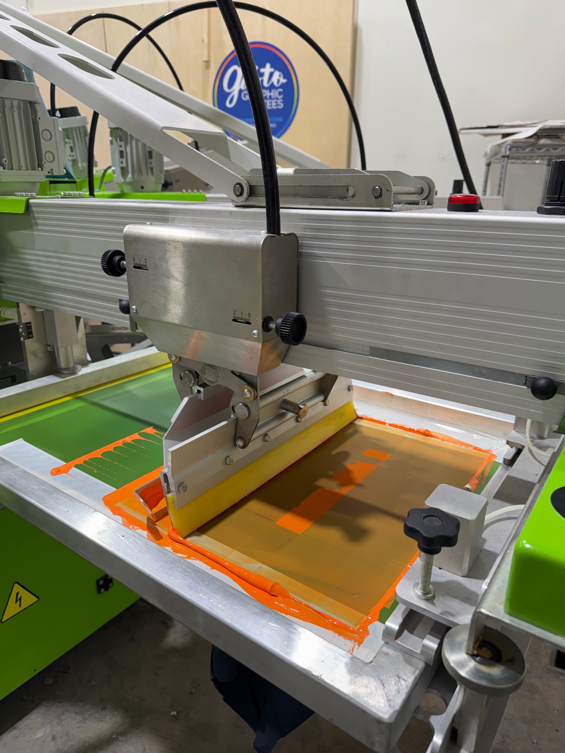 Close-up of a ROQ auto screen printer with a yellow component on a green surface