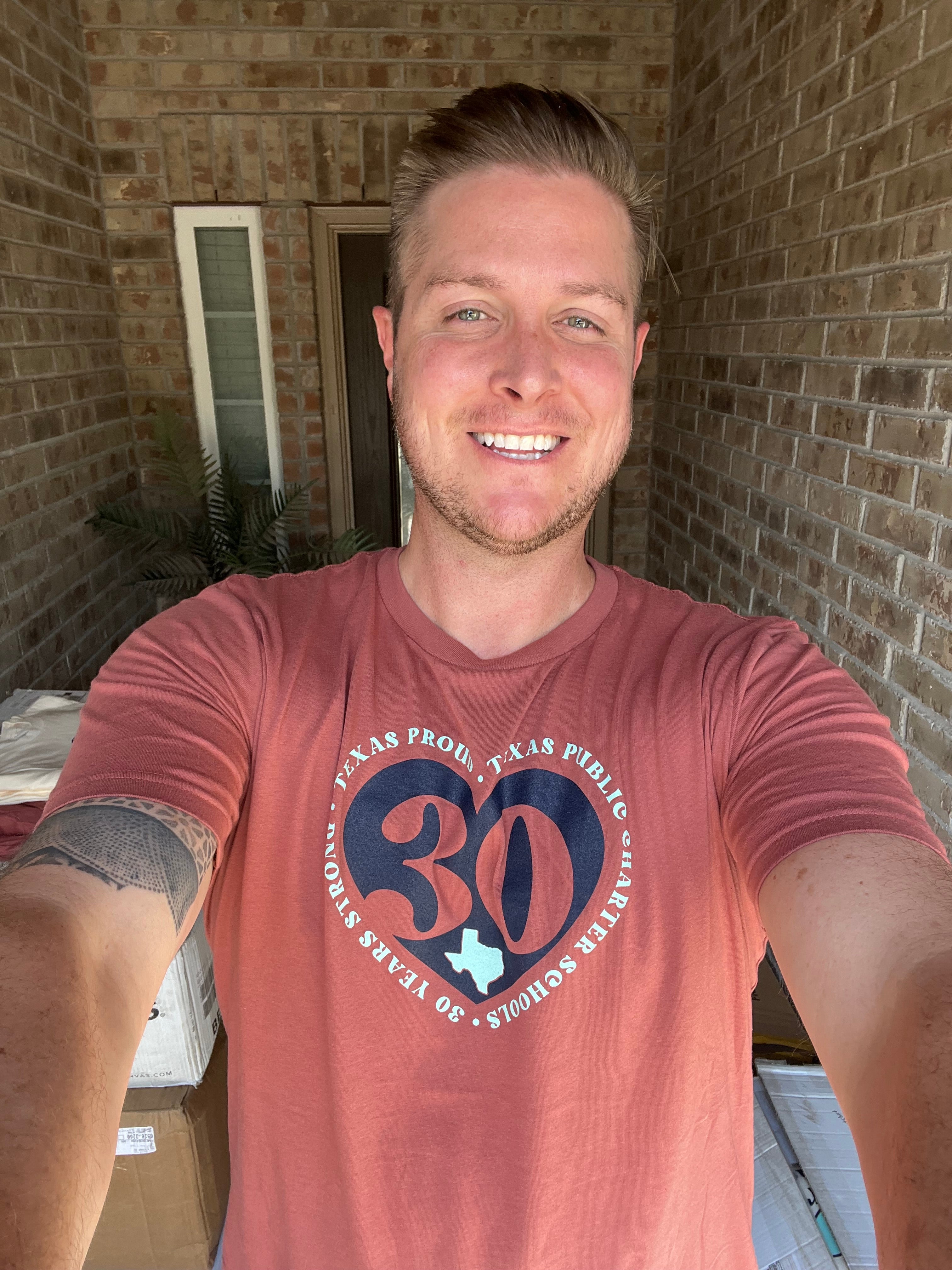 Man wearing a red t-shirt with a logo, standing in front of a brick wall.