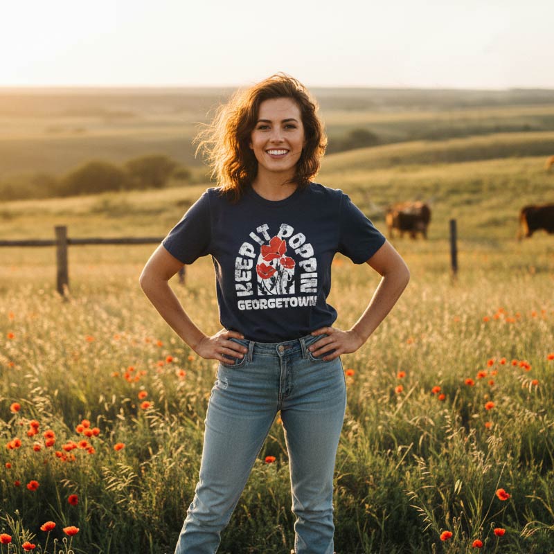 Woman wearing a t-shirt with a graphic design standing in a field with cows and flowers.