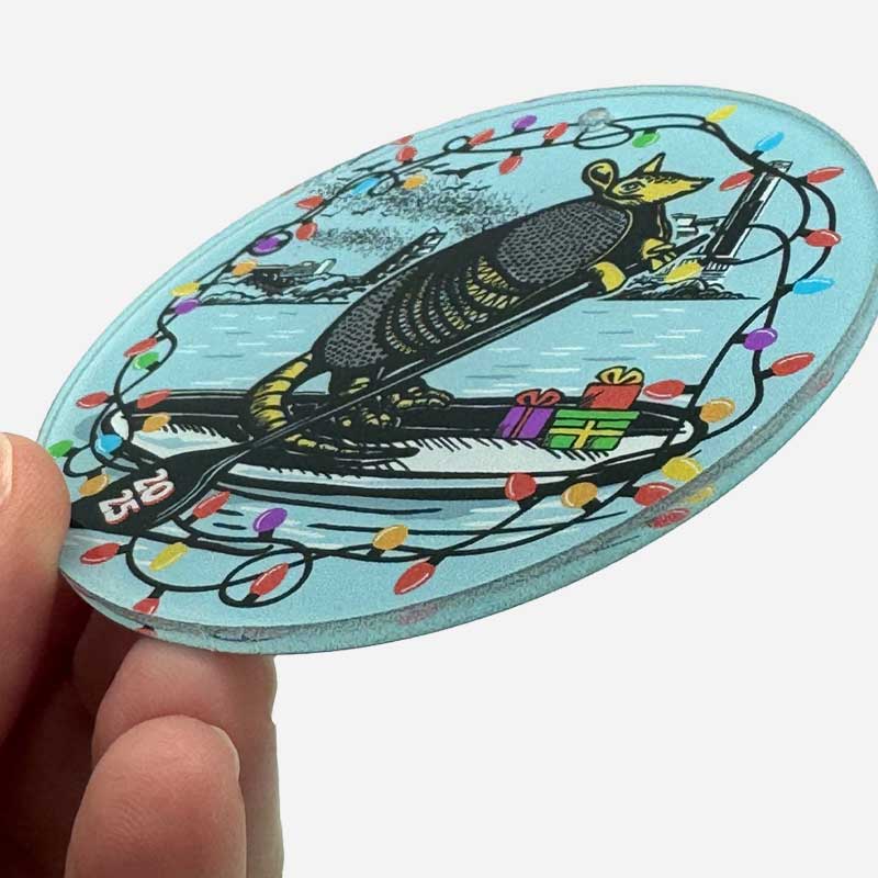 Decorative Christmas ornament with Festive armadillo paddle boarding on Lady Bird Lake with a Christmas light border.