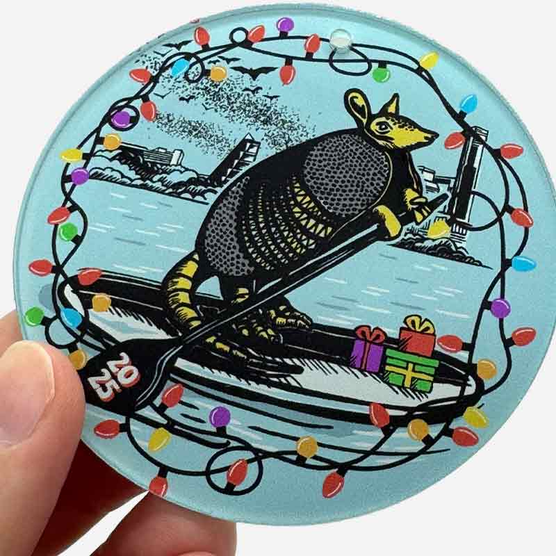 Ornament with an armadillo design surrounded by Christmas lights and presents, held in a hand.
