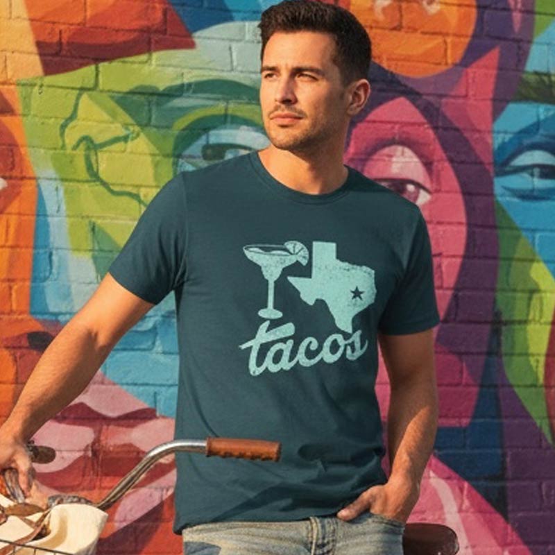 Man wearing a t-shirt with a Texas and tacos design, standing in front of a colorful mural.
