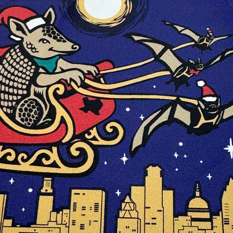 Armadillo in Santa’s sleigh flying over the Austin skyline with bats leading the way.