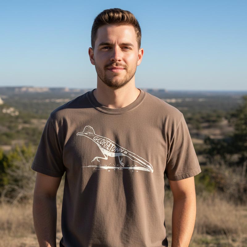 Man wearing a brown GTX Roadrunner t-shirt standing outdoors with a scenic background
