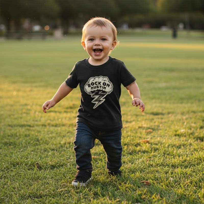 Child wearing a black t-shirt with 'Rock on Austin' design in a park