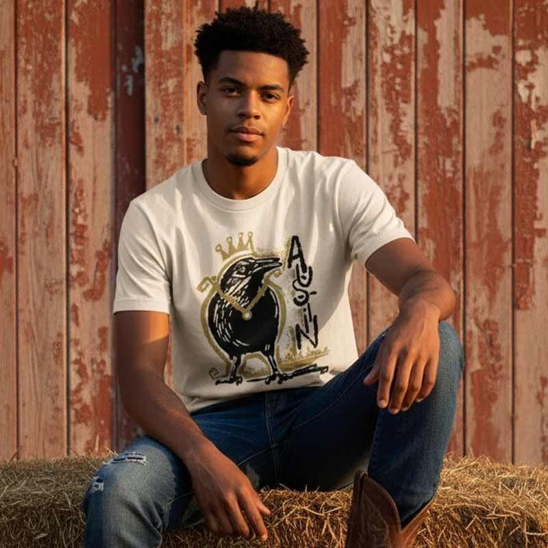 Man wearing a white t-shirt with a graphic design sitting on hay against a wooden fence.