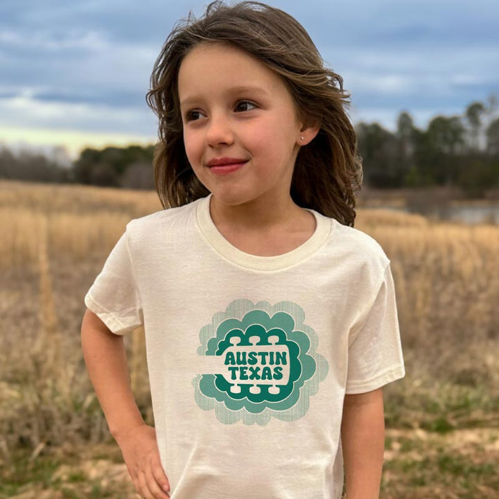 Model wearing our Sky Sync youth t-shirt with guitar neck rising into clouds – Austin music-themed tee for kids