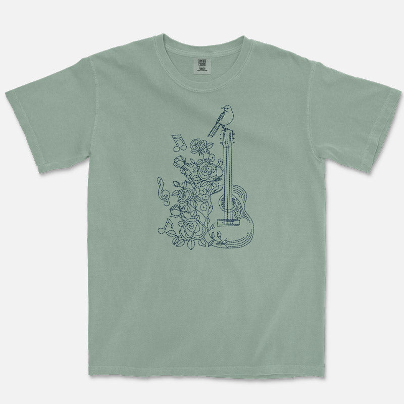 Green t-shirt with floral and guitar design on a white background