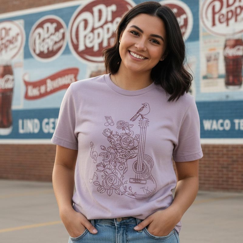 Woman wearing a purple t-shirt with a guitar and floral design in front of a Dr Pepper sign.