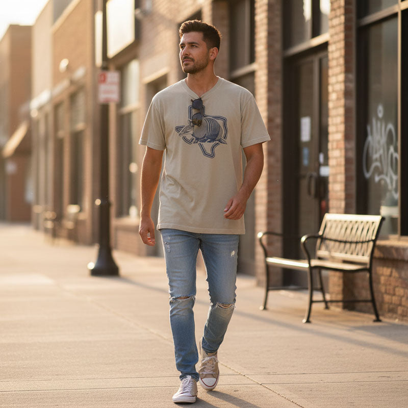 Man walking on a sidewalk wearing a beige t-shirt and blue jeans.
