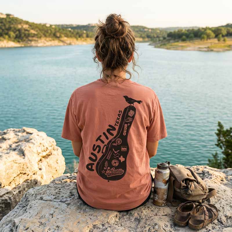 Woman wearing Carry-On Austin terra cotta Comfort Colors t-shirt sitting by Lake Travis Austin Texas