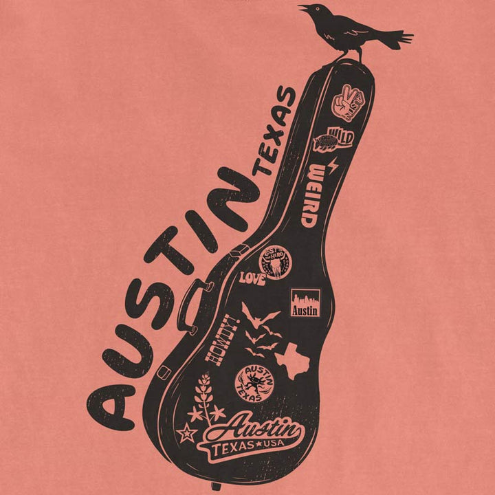 Details of Terracotta Comfort Colors 1717 Carry-On Austin t-shirt laid flat with Austin-inspired accessories including sunglasses, guitar picks, and travel-inspired details. Front graphic features a guitar case covered in Austin stickers and a grackle.