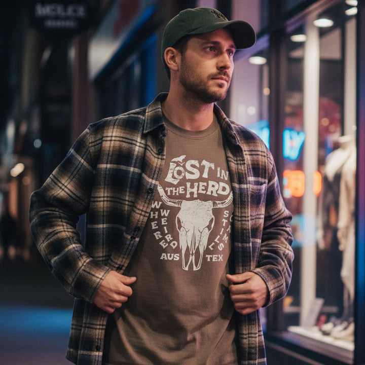Man wearing a plaid shirt over a graphic t-shirt with text and design, standing on a street at night.